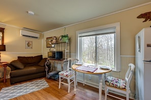 A cozy living room with a sofa, a dining table, chairs, a TV, and a window with a view. - BabyBears Peaceful cabin & hot tub (Whittier)