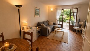 Uma sala de estar acolhedora com um sofá, uma mesa de jantar com cadeiras, um abajur e uma janela com cortinas.