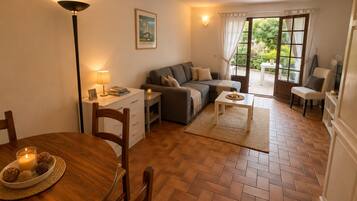 Un salon confortable avec un canapé, une table à manger et des chaises, une lampe et une fenêtre avec des rideaux.