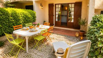 Une terrasse extérieure avec une table dressée pour le repas, entourée de chaises, et une porte donnant accès à un bâtiment.