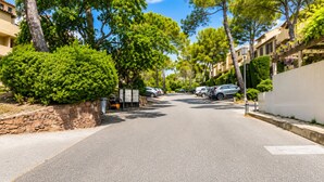 Rua residencial com carros estacionados, muros de pedra e árvores.