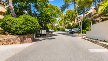 Une rue résidentielle bordée de voitures garées, de murs en pierre et d’arbres.