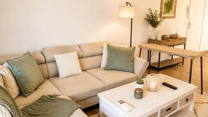 Olohuoneessa on beigenvärinen sohva, sohvapöytä, lamppu, sivupöytä ja seinällä oleva kehystetty taulu.