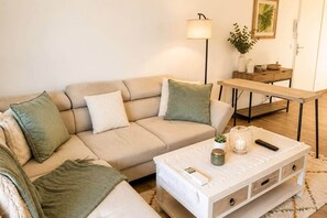 Ein Wohnzimmer mit einem beigefarbenen Sofa, einem Couchtisch, einer Lampe, einem Beistelltisch und einem gerahmten Bild an der Wand.