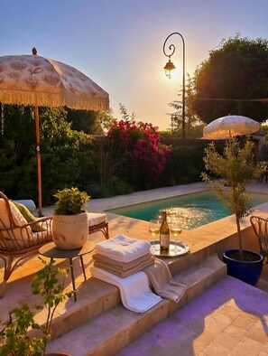 A poolside area with a chair, umbrella, potted plants, and a bottle of wine. - La Maison de la Tour (Léré)
