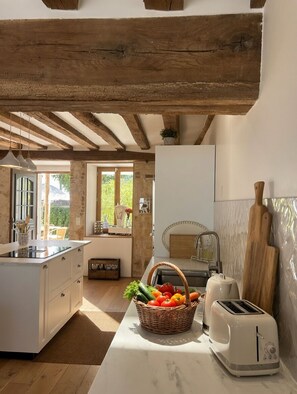 A kitchen with a wooden ceiling, a white countertop, a toaster, and a basket of fruit. - La Maison de la Tour (Léré)
