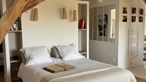 A bedroom with a large bed, wooden beams, a bookshelf, and a mirror. - La Maison de la Tour (Léré)