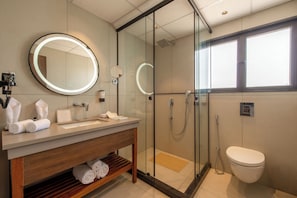A modern bathroom with a glass-enclosed shower, a round mirror with a light, a wooden vanity, and a toilet. - Tree of Life Ganga Dwar Haridwar (Haridwar)
