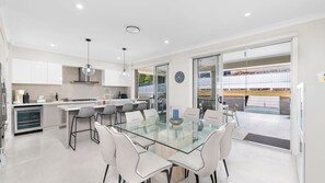 A modern kitchen with white cabinets, a glass dining table, and a view of the outdoors. - 3 Ebbtide Way, Corlette (Corlette)