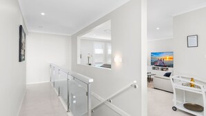 Een modern interieur met een glazen balustrade, een bank en een televisie waarop een zonsondergang te zien is.