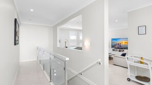 A modern interior with a glass railing, a sofa, and a TV displaying a sunset scene. - 3 Ebbtide Way, Corlette (Corlette)
