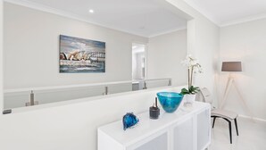 Een moderne hotellobby met een witte receptiebalie, een schilderij van een brug, een potorkidee en een vloerlamp.