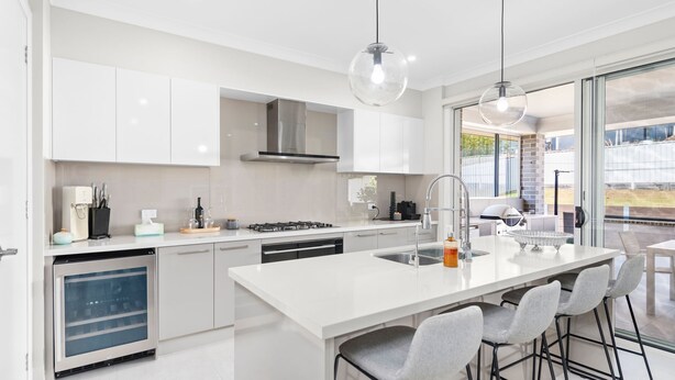 Een moderne keuken met witte kasten, een centraal eiland met barstoelen, een ingebouwde vaatwasser en een groot raam met uitzicht op de omgeving.