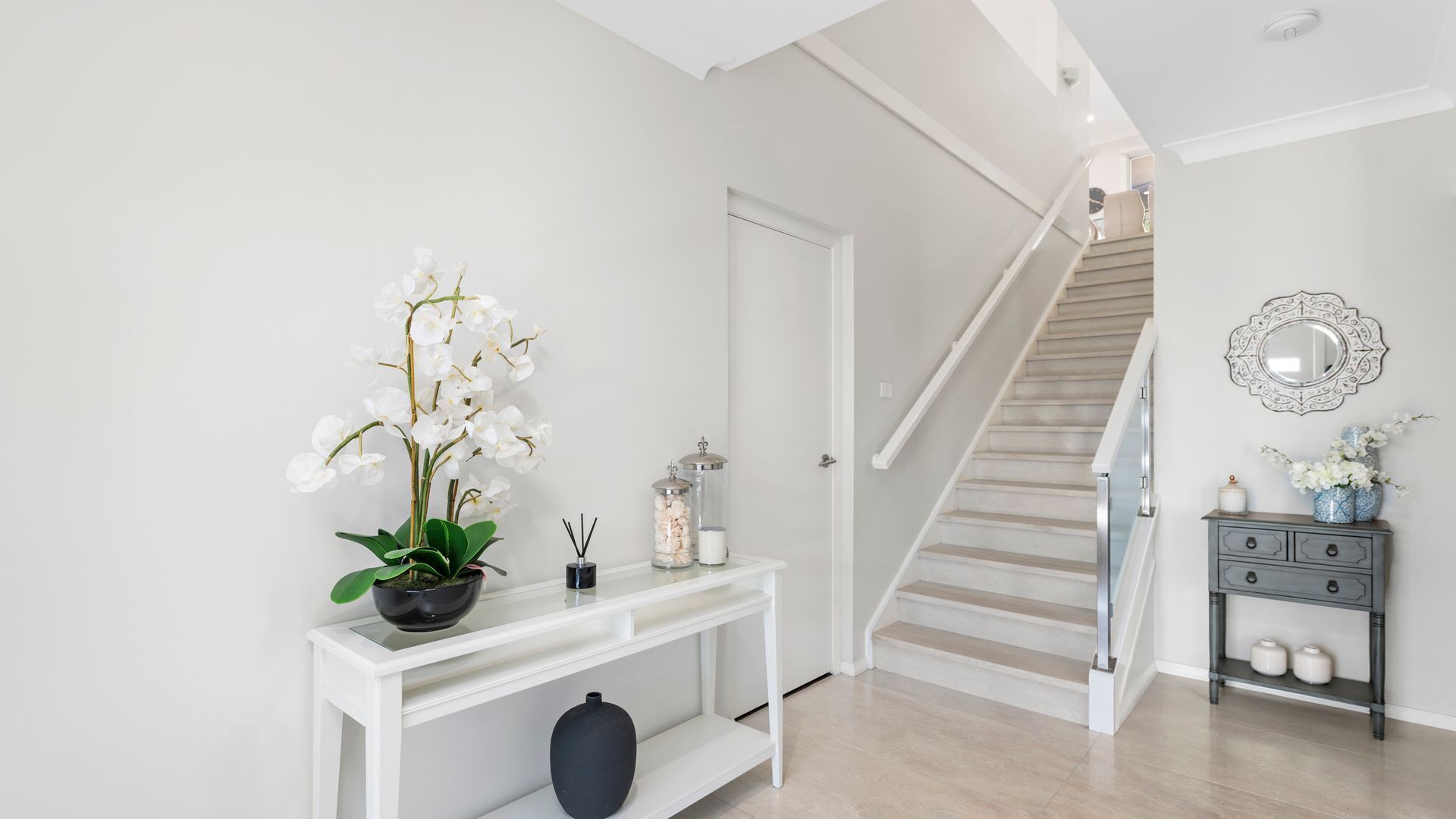 Eine Treppe führt zu einer zweiten Etage, ein weißer Konsolentisch mit einer Orchidee im Topf und ein dekorativer Spiegel an der Wand.