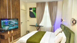 A hotel room with a bed, a TV, a small table, and curtains. - Eleven Apartments (Galadimawa)