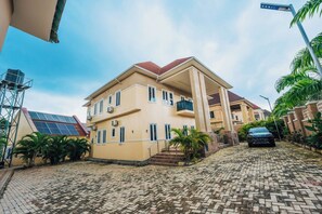A residential building with a sloped roof, a car parked in the driveway, and solar panels on the roof. - Eleven Apartments (Galadimawa)