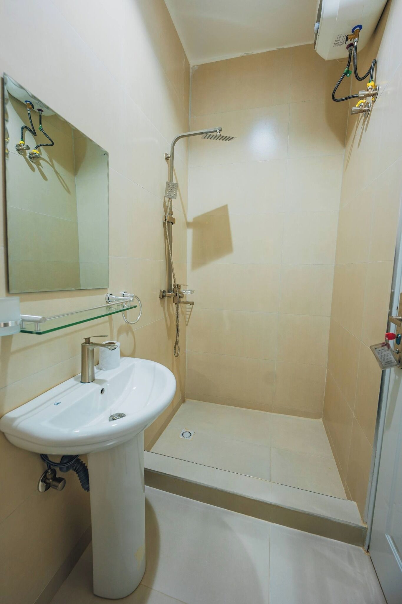 Une salle de bain avec un lavabo sur colonne, une étagère en verre, une douche et un miroir.