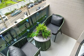 A balcony with two chairs, a small table with a plant, and a view of the street below. - Eleven Apartments (Galadimawa)