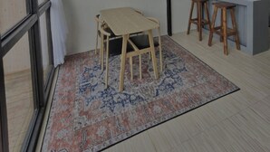 A room with a wooden table, two stools, a hanging light fixture, and a patterned rug.
