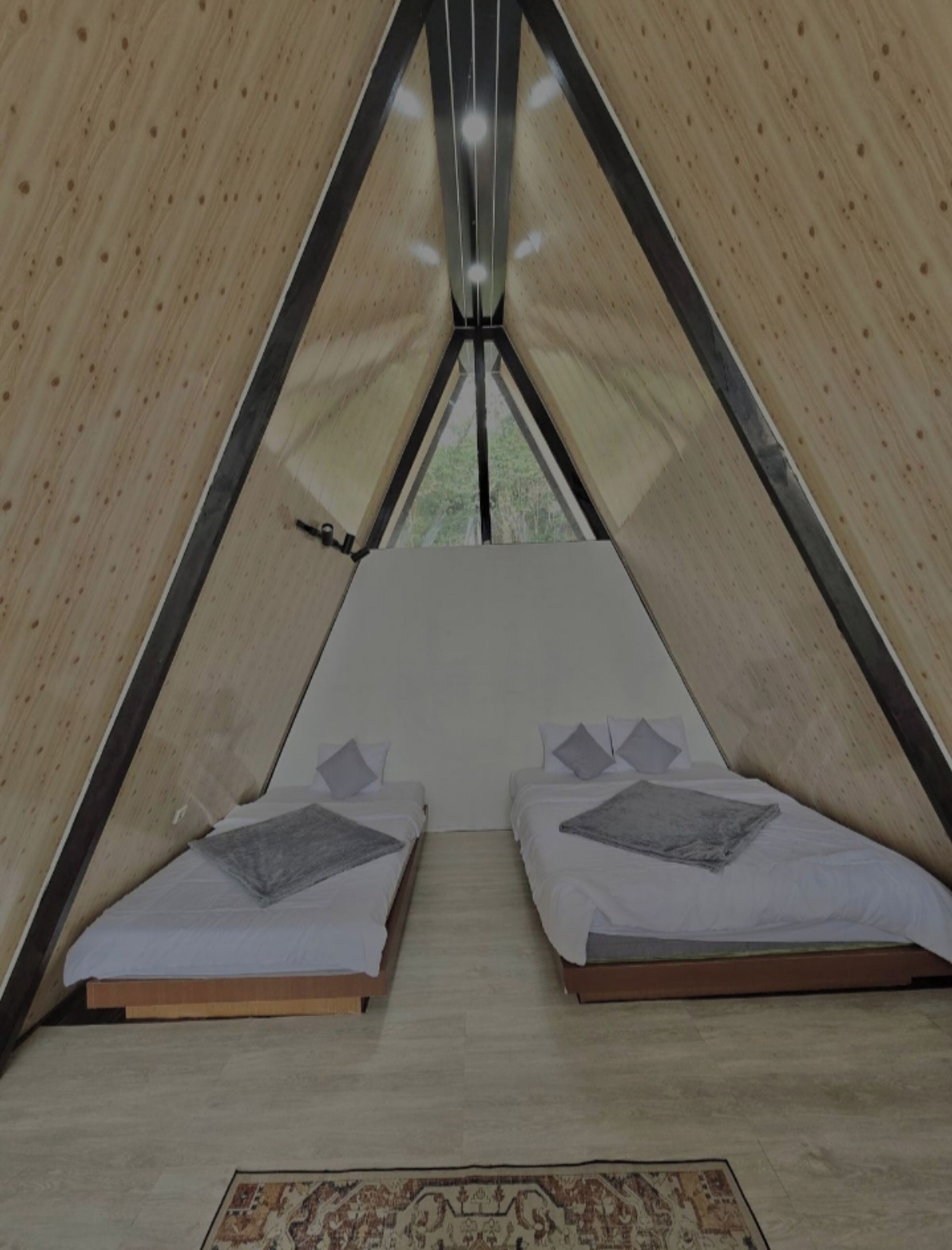 A tent with two beds, a rug, and a view of trees outside.