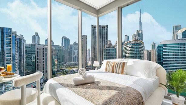 A modern hotel room with a large bed, a dining table with breakfast, and a city view. - Luxury Burj Khalifa & Canal View Studio (Dubai)