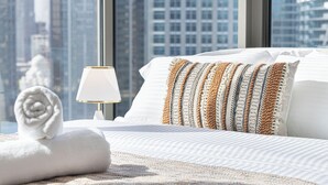 A hotel room with a bed, a rolled towel, a lamp, and a view of a cityscape through large windows. - Luxury Burj Khalifa & Canal View Studio (Dubai)