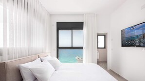 Een hotelkamer met een bed, een televisie aan de muur en uitzicht op zee.