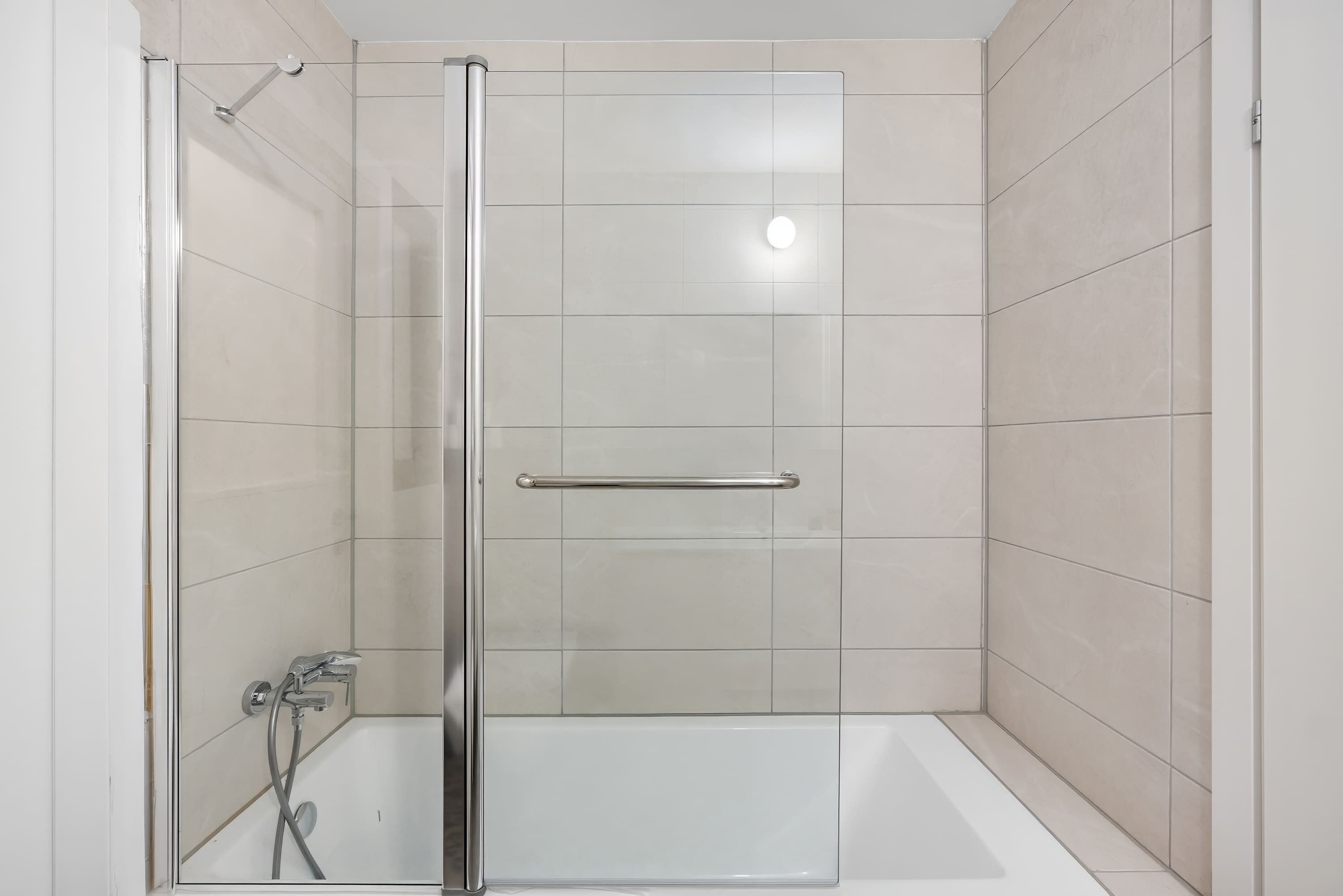 A modern bathroom with a glass-enclosed shower, a white bathtub, and a handrail.