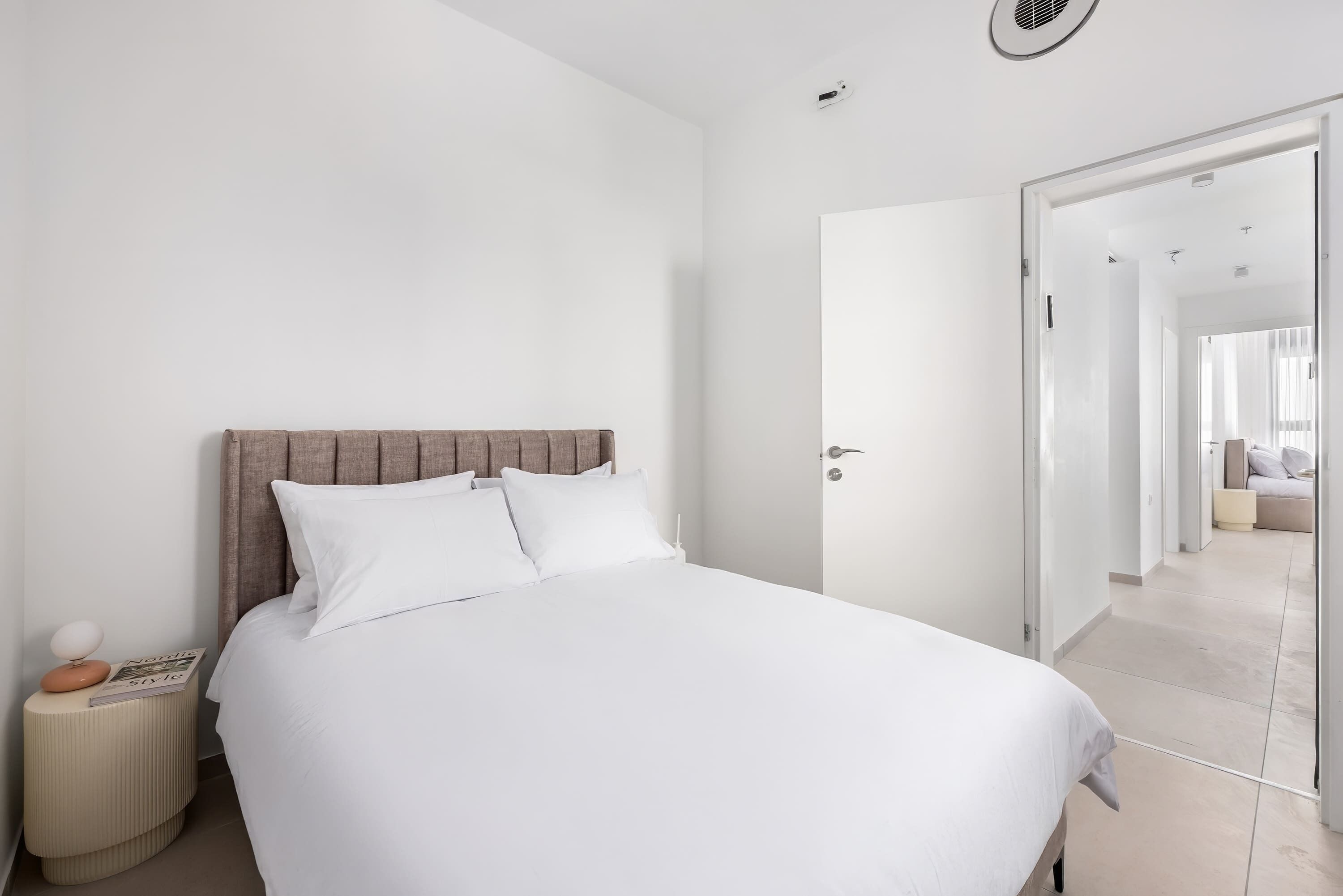 Une chambre moderne avec un grand lit, une table de chevet et une porte donnant sur une autre pièce.