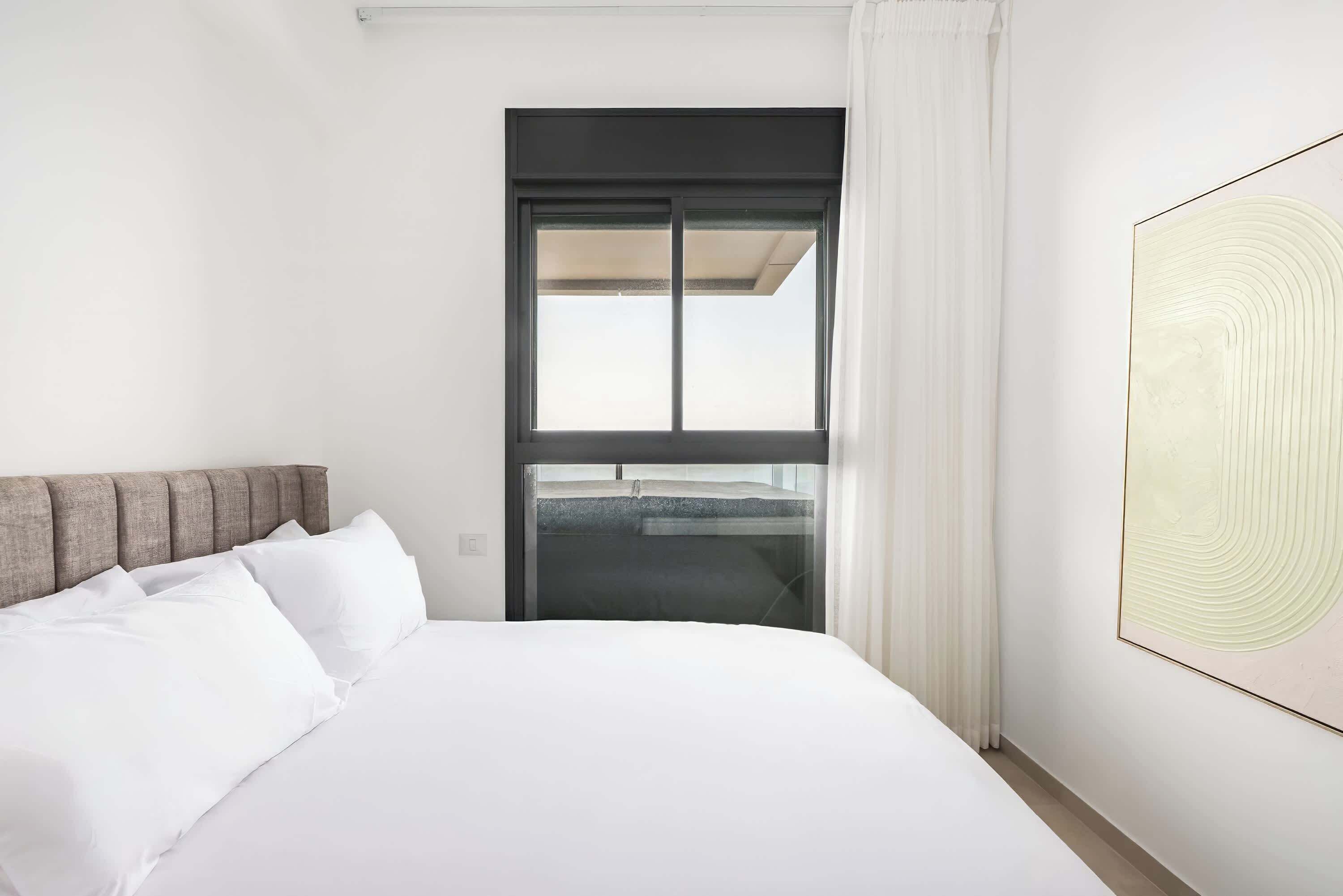 Habitación de hotel con cama, ventana con cortinas, un cuadro en la pared y vistas al exterior.