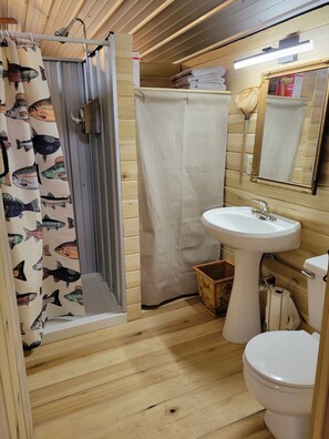 A bathroom with a shower, a sink, and a toilet. - Cabin #1 Cozy "fishing" themed cabin by the creek. Recently featured in magazine (Linden)