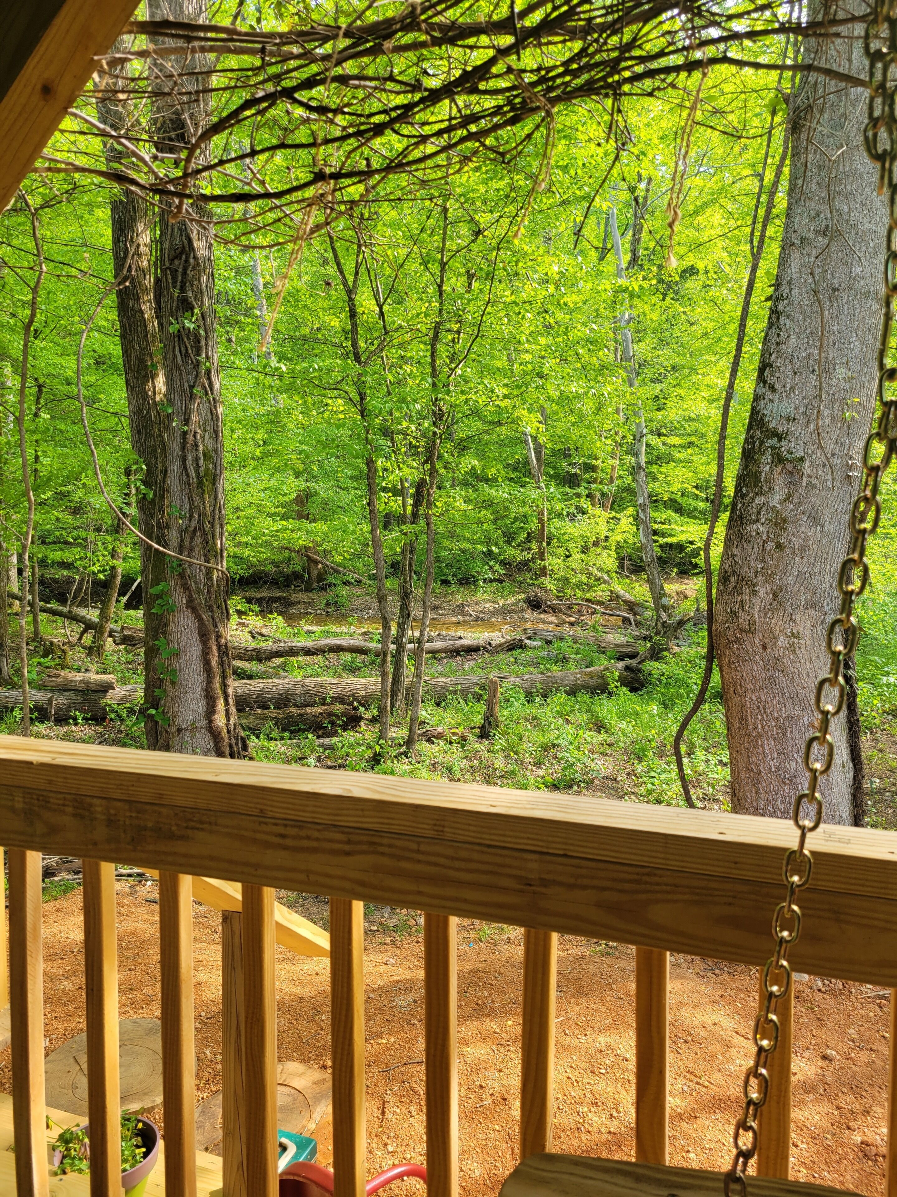 A wooden deck with a chain-link railing overlooking a forested area.. Cabin #1 Cozy "fishing" themed cabin by the creek. Recently featured in magazine