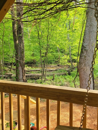 A wooden deck with a chain-link railing overlooking a forested area.. Cabin #1 Cozy "fishing" themed cabin by the creek. Recently featured in magazine