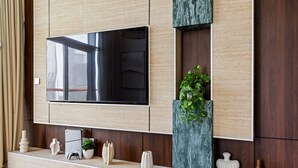 Ein modernes Wohnzimmer mit einem großen Flachbildfernseher an einer Holzwand, einer Zimmerpflanze und einem Konsolentisch mit verschiedenen Gegenständen.