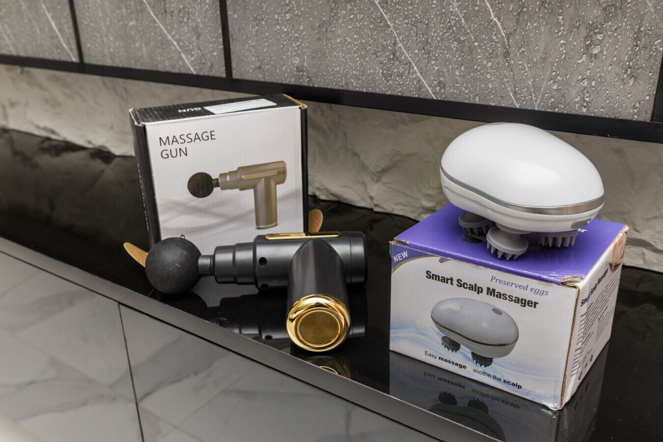 A massage gun, a smart scalp massager, and their packaging on a countertop.