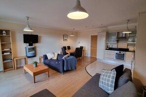 A modern living room with a sofa, coffee table, TV, and dining area.