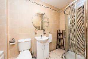 A bathroom with a toilet, sink, mirror, shower, and tiled walls.