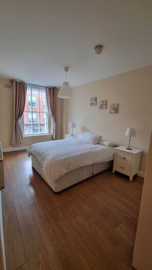 A bedroom with a bed, bedside tables, a window with curtains, and a ceiling light.