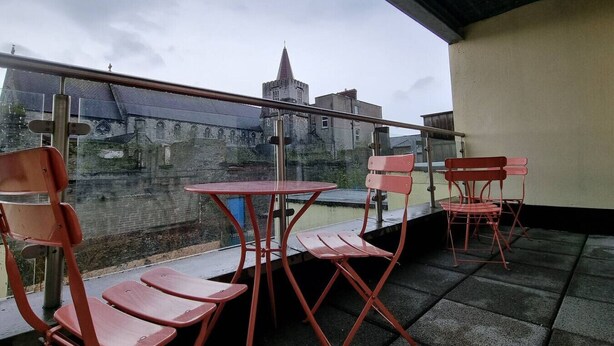 A balcony with red chairs and a table, overlooking a historic building with a tower. - Spacious 2 Bed Apartment w/balcony (Dublin 8)