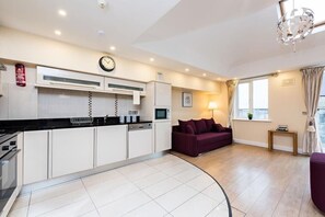 A modern kitchen with white cabinets, a black countertop, and a clock on the wall.