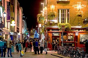 Een nachtelijk straatbeeld met diverse winkels en een opvallende bar genaamd 'The Temple Bar'.