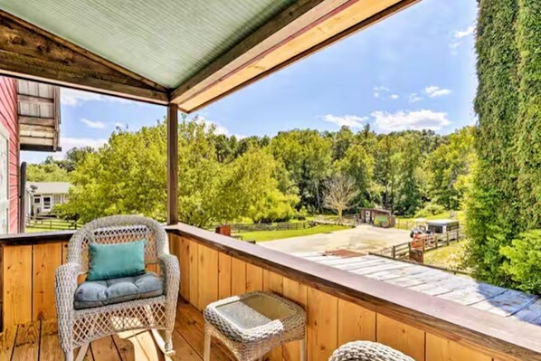 Una terraza de madera con mobiliario de mimbre, una vista despejada de un paisaje verde y un edificio distante.