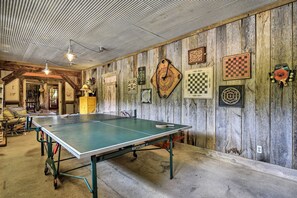 Una mesa de ping pong en una habitación rústica con paredes de madera y varios juegos de mesa.