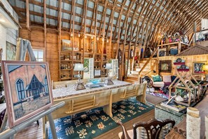 Un interior rústico de madera con techo alto, una mesa de comedor central y una escalera que conduce a un nivel superior.
