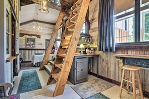 A rustic interior with exposed wooden beams, a staircase, a kitchen area, and a bar.