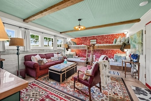 A cozy room with a bunk bed, a red sofa, a wooden chest, and a patterned rug.