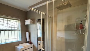 Ein modernes Badezimmer mit einer Duschkabine aus Glas, einem weißen Waschbecken, einer Toilette und einem Mülleimer.