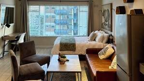Ein modernes Wohnzimmer mit Bett, Sofa, Esstisch und Kühlschrank.