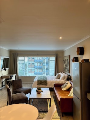 Ein modernes Wohnzimmer mit Bett, Sofa, Esstisch und Kühlschrank.