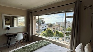 Ein Schlafzimmer mit einem großen Bett, einem Schreibtisch und einem Fenster mit Blick auf die Stadt.